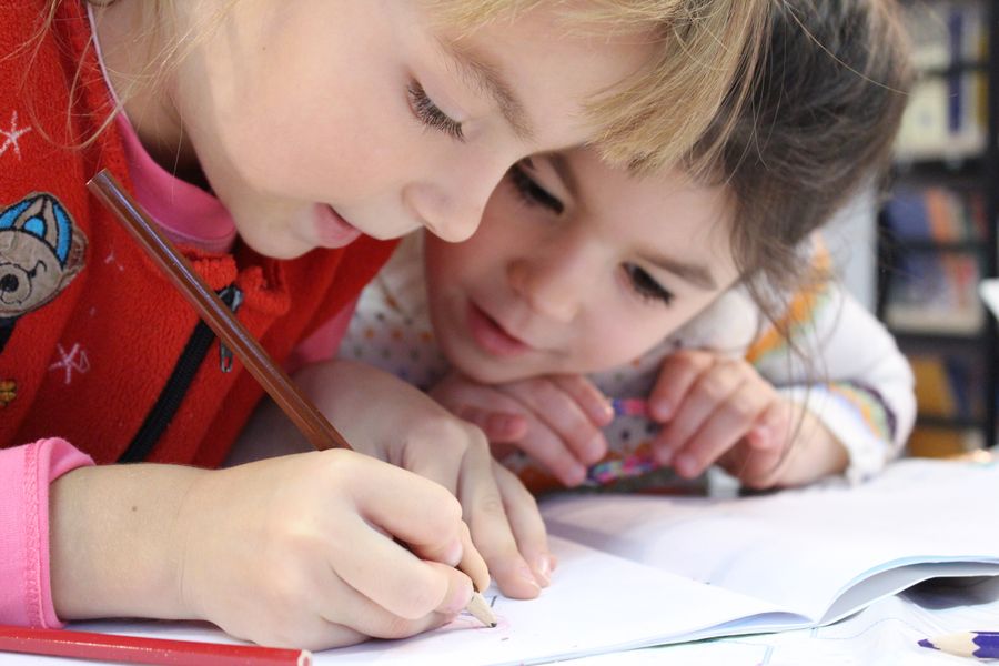 Two children leaning over a page, drawing with a pencil