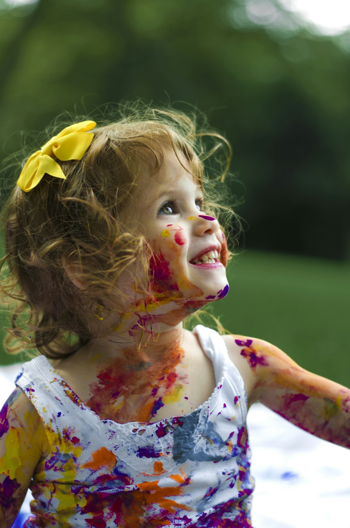 A smiling child with paint on her cheeks, looking upward