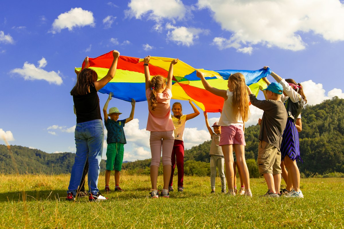 Children holding a rainbow parachute in a field