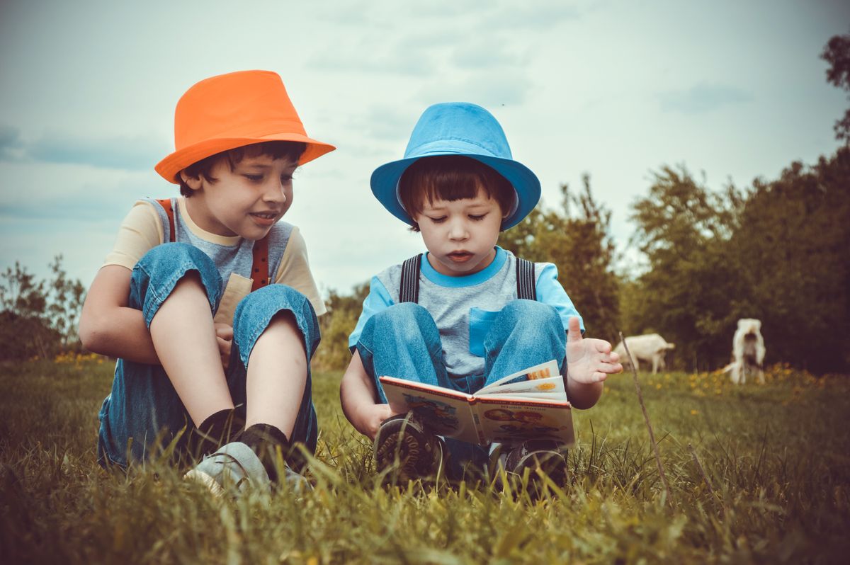 Two children reading a book while sitting in the grass