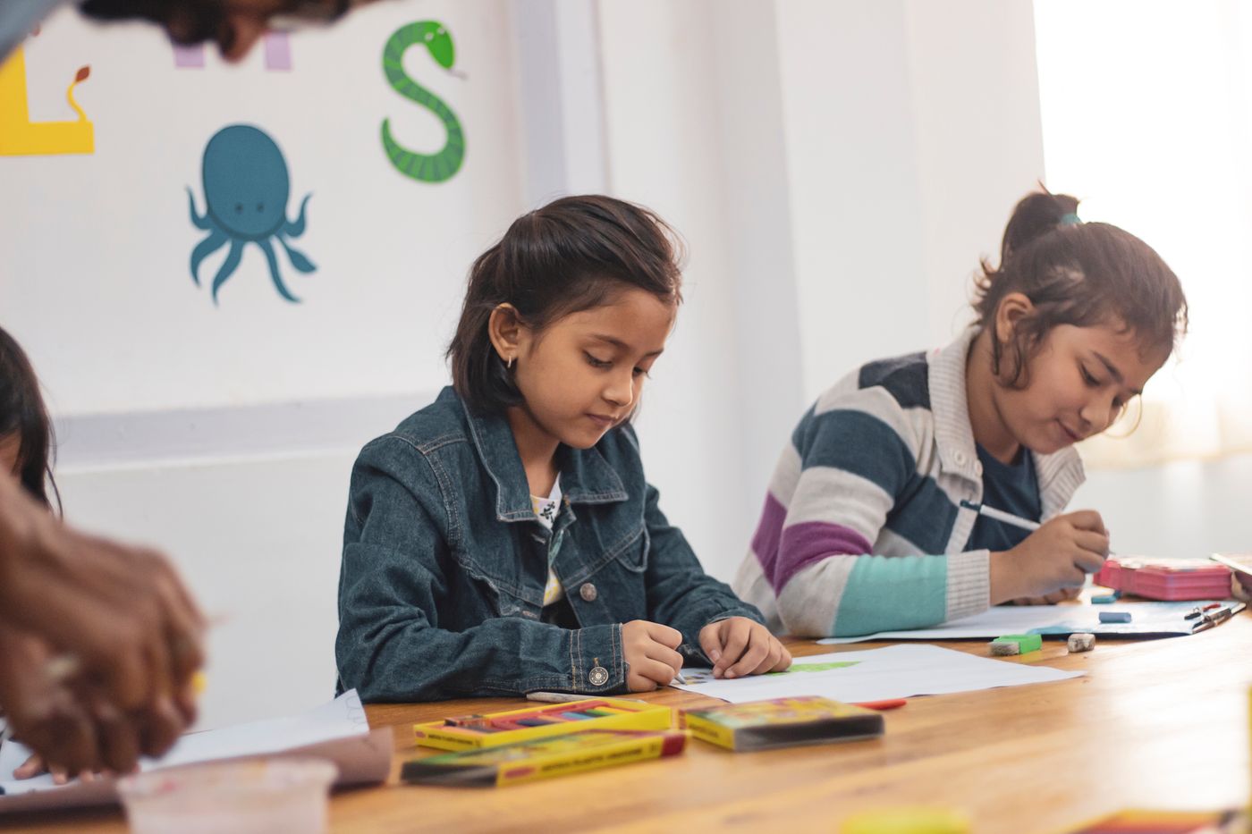 Two girls drawing with crayons at a classroom table