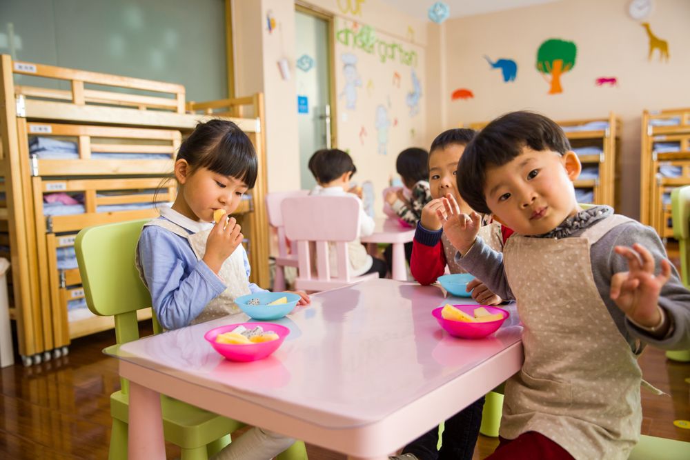Children at a kindergarten table with bowls of fruit